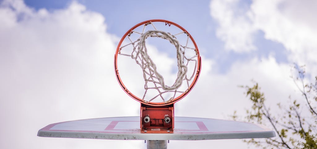 Low angle of modern basketball hoop on backboard against cloudy sky on sports ground